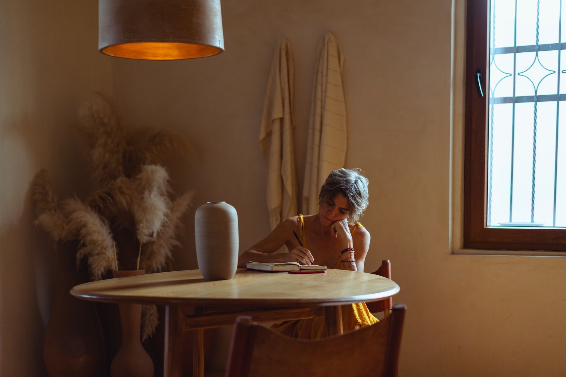 A senior woman enjoys journaling at a table in a warm, cozy home setting
