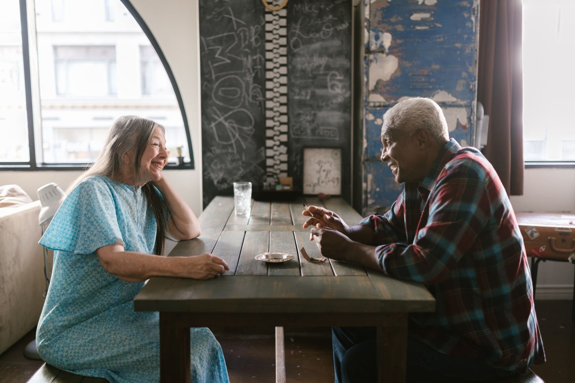 Two adults enjoying a cheerful conversation over a table in a warm, cozy indoor setting